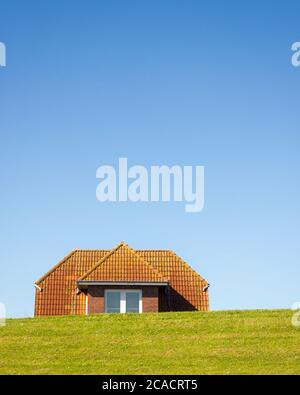Close up shoot of a dike in the German north-sea region with a house directly behind. Only the roof overlooks the dike. It seems both, the house is sa Stock Photo