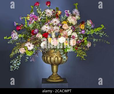 A Beautiful large flower bouquet with a lot of different flowers in a golden pot, on a blue background Stock Photo