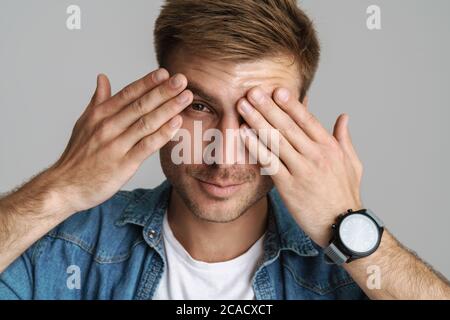 Portrait of pleased unshaven man smiling and covering his eyes isolated over grey background Stock Photo
