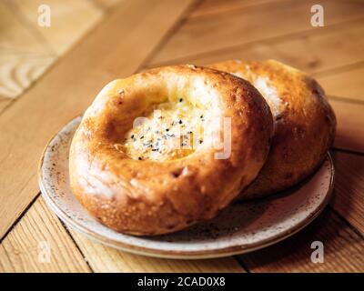 Tasty fresh tandoor bread on rustic wooden tabletop. Two tandoor flat bread cake with black sesame seeds on yellow wooden table background. National asian meal and food Stock Photo