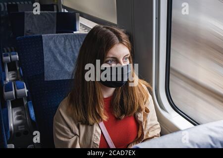 Young woman wearing protective face mask travelling by traing. Stock Photo