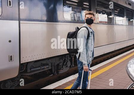 Young man wearing protective face mask standing on the railway station near the train Stock Photo