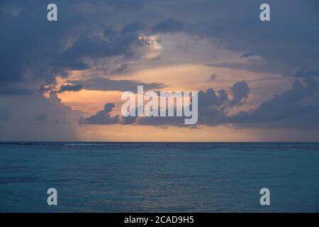 orange sunrise in cloudy blue sky of maldives. Blue peaceful ocean waves on horizon Stock Photo