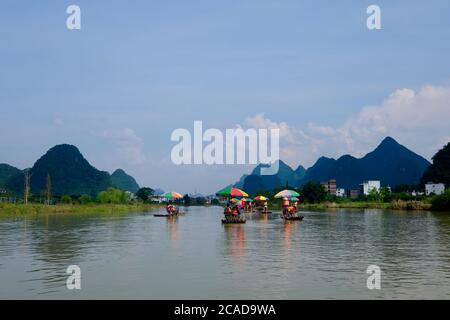 Several bamboo rafts floating on wide river. Blue mountains and blue sky with white clouds. In Yangshuo Guilin China. Karst landform Stock Photo