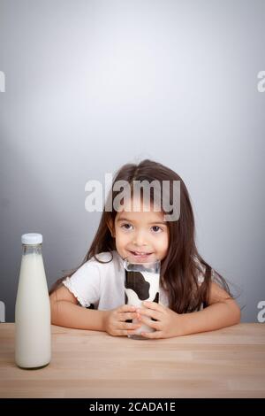 Adorable baby girl holding glass of milk and drinking milk Stock Photo