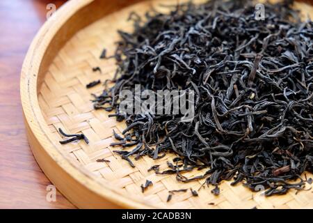 close up heap of dry tea leaves in yellow bamboo plate. Blur background. traditional Chinese tea culture concept Stock Photo