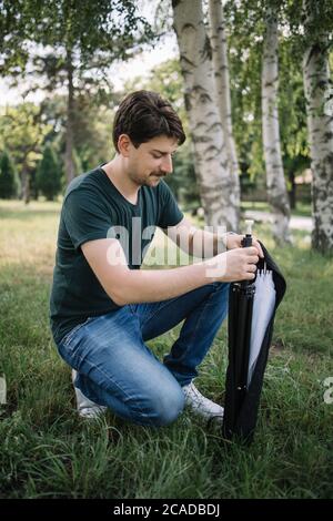 Young man holding camera stand while squatting in forest Stock Photo