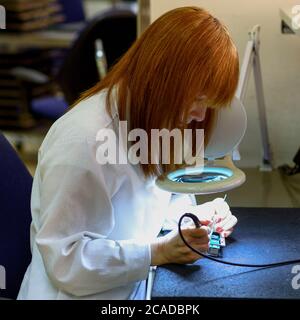 Woman Soldering a circuit board in her tech office.Close up of female engineer Middle-aged quality inspector is checking the item. Testing and fixing a circuit board. Stock Photo