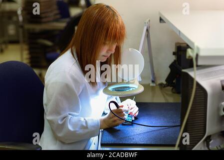 Woman Soldering a circuit board in her tech office.Close up of female engineer Middle-aged quality inspector is checking the item. Testing and fixing a circuit board. Stock Photo