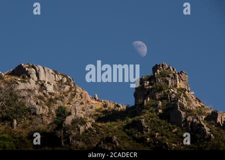 An half moon rises behind mountain peak at the end of day. Close up shot Stock Photo