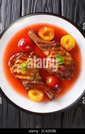 grilled pork chop with ripe plums and sauce close-up in a plate on the table. Vertical top view from above Stock Photo