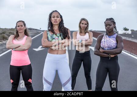 Group of serious diverse ladies with crossed arms standing on road and looking at camera during running training in outskirts Stock Photo