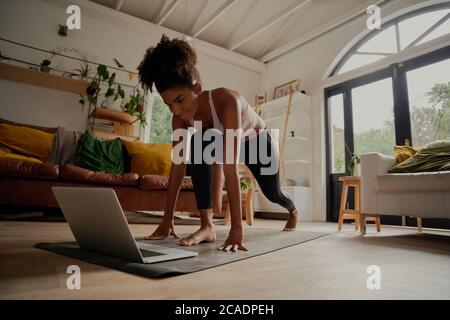 Happy woman watching video on laptop while exercising on yoga mat at home - lock down workout Stock Photo