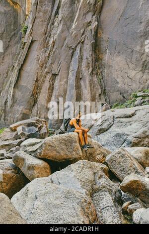 Young man resting on boulder, observing Yosemite Falls. Stock Photo