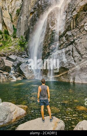 Young man standing on boulder, observing Yosemite Falls. Stock Photo
