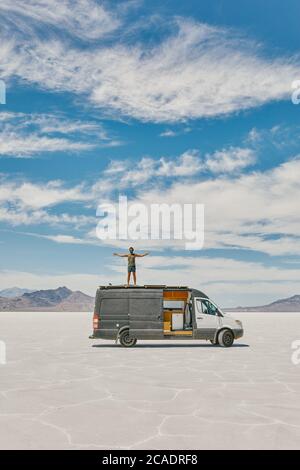 Young man standing on roof of camper van in Bonneville Salt Flats. Stock Photo