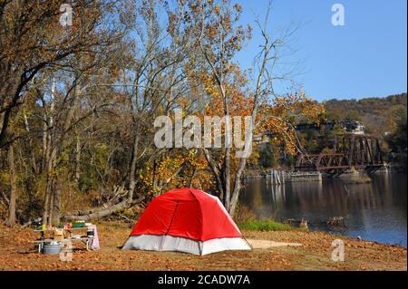 Red tent is set up next to a picnic table on the shore of Table Rock Lake in North Arkansas.  Eureka Springs and North Arkansas Railway bridge sits in Stock Photo