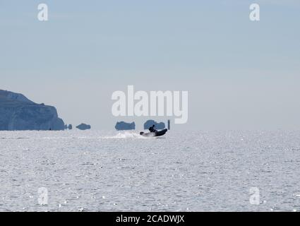 Small inflatable rib with one person crossing in front of the Needles located on the western end of the Isle of Wight, UK Stock Photo