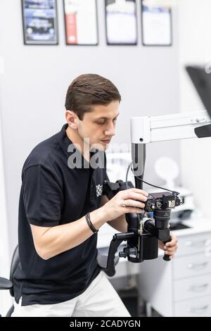 Mature stomatologist posing on workplace, near dental microscope, leaning on dentist chair. Handsome, bearded stomatologist wearing in white medical c Stock Photo