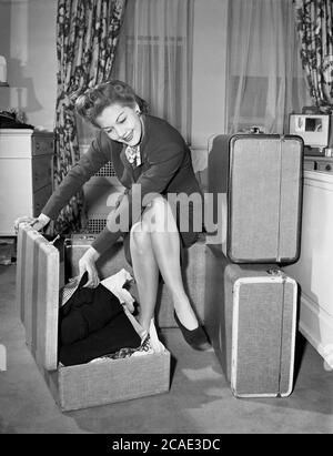 1940s, historical, attractive, well-dressed lady sitting in a hotel room with her clothes packed in three traditional box or hard sides suitcases. These types of suitcases were more portable than trunks, but stil bulky by modern standards, being cloth bound over a rigid wooden frame, but offered a high level of security as it could not be opened quickly. Stock Photo