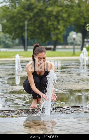 Attractive girl happily plays with fountain water stabs in city park. Stock Photo