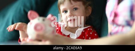 Mom and daughter sit home on couch with piggy bank Stock Photo