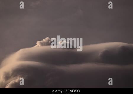 Large gray cumulus clouds almost entirely covered by pileus, floating under a cloudy sky. Stock Photo