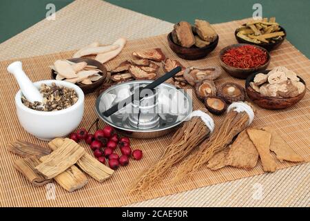 Chinese herbal medicine selection and moxa stick used in moxibustion therapy with mortar and pestle on bamboo mat and mottled green background. Stock Photo