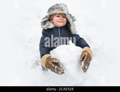 Cute child standing in winter hat with red nose. Joyful kid Having Fun and making snowman in Winter Park. Winter clothes for kids. Stock Photo