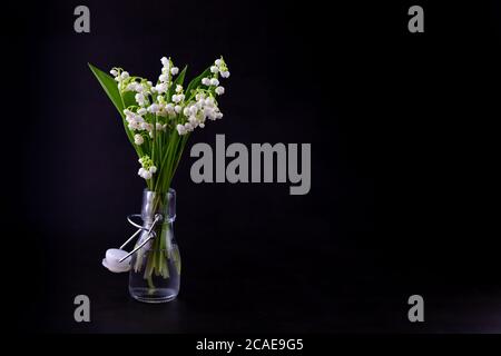 A bouquet of lilies of the valley on a black background with place for text. Delicate white spring flowers. Bouquet in a glass bottle. Copyspace. Stock Photo