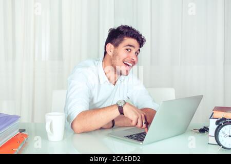 Happy adult man looking excitedly at camera while pushing enter button on laptop keyboard at table in office. Nerdy programmer hacker coder girl about Stock Photo