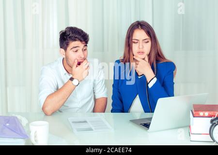 Young bored man and concerned woman couple colleagues in disbelief sitting at desk, watching laptop with strong emotions at table in office living roo Stock Photo
