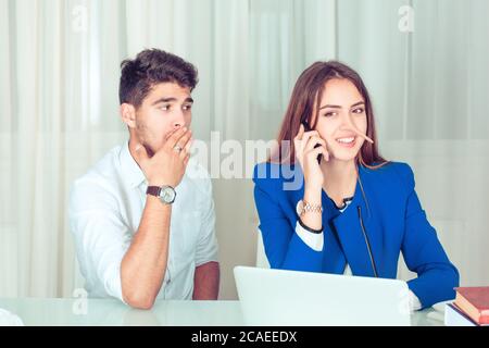 Young woman with long nose cheating and telling lies while having call and man looking shocked while sitting near in the office at workplace, home at Stock Photo