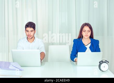 Modern young calm and serious man and woman sitting at table and using laptops working in office together with a vacant place between them. We need em Stock Photo
