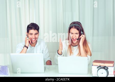 Young angry screaming woman and cheerful man using computers and talking to clients coworking in office, call service center at laptops. Different app Stock Photo