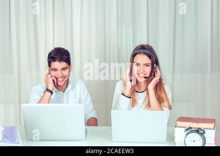 Cheerful man and woman working in call service and sitting at table with laptops talking with customers. Happy polite customer service representatives Stock Photo
