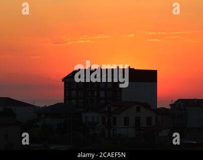 Sun setting behind a 1970's ugly block of flats in Cueto Cantabria Spain Silhouetted buildings with strong orange sunlight and an ocean horizon Stock Photo