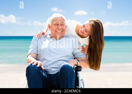 Happy Young Woman With Her Old Senior Father On Wheelchair On Vacation Stock Photo