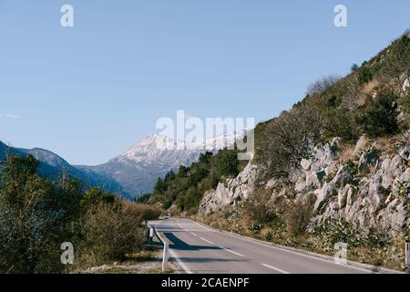 Mountain serpentine road with a car driving in the opposite direction overlooking the mountains and blue sky. Stock Photo