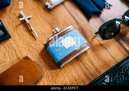 Close-up of a male blue jar with brown leather inserts with a purse, sunglasses and a cross on a smooth wooden surface. Stock Photo