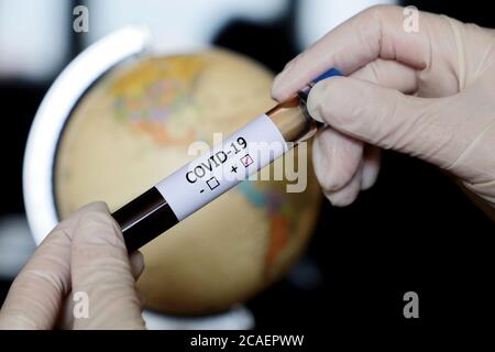 Test tube with covid-19 blood sample in female hands on globe background. Doctor or scientist with positive coronavirus test, pandemic in world Stock Photo