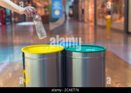 Woman putting empty plastic bottle in recycling bin in the mall. Different trash can with colorful garbage bags. Stock Photo