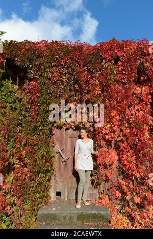 Mature happy beautiful woman against suburban house covered in autumn leaves Stock Photo