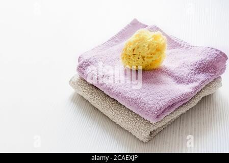 A natural yellow sponge on towels stacked on a white wooden table. Personal care and hygiene. Bath and relax Stock Photo
