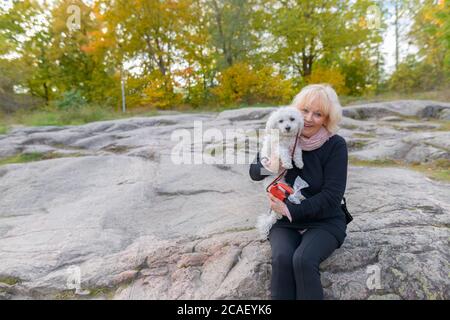 Senior happy woman smiling while holding her pet dog sitting on boulder in the mountains Stock Photo