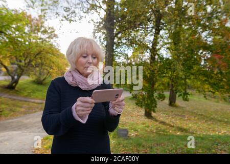 Senior woman holding mobile phone on the path of quiet and relaxing natural park Stock Photo