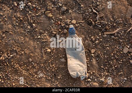 an old plastic bottle lies on  ground, yellow sand and stones on lifeless earth,  crumpled bottle thrown by people, environmental pollution, garbage i Stock Photo