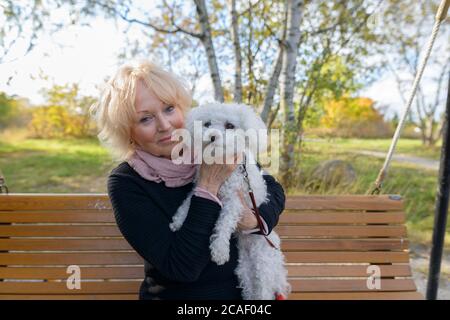 Senior woman holding her pet dog while sitting on wooden bench with natural scenic view of the park Stock Photo