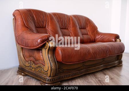 brown vintage oak leather sofa stands in room with white walls, sofa with patterns, beautiful furniture comfortable sofa Stock Photo