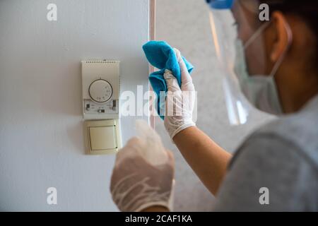 Cleaning in hotel or hospital. Hands in gloves cleaning and disinfecting elevator buttons and doors using alcohol sanitizer spray. Back view. Disinfec Stock Photo